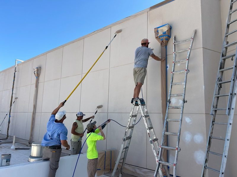 The 9 & Contractors crew painting a commercial building exterior from ladders and extension rollers.